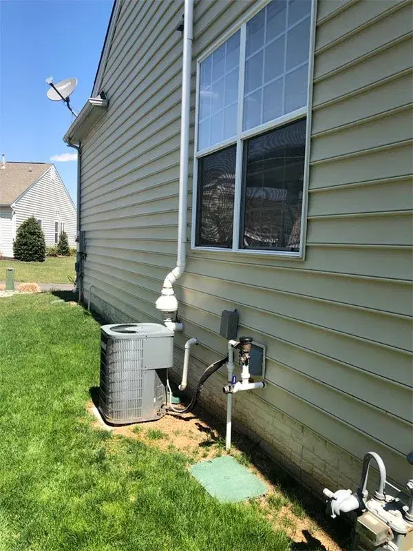 HVAC air conditioning unit installed outside residential home with white vinyl siding and electrical connections