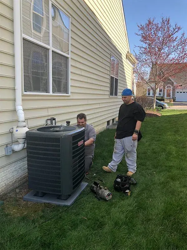 Two HVAC technicians installing a new air conditioning unit outside home with professional equipment and tools